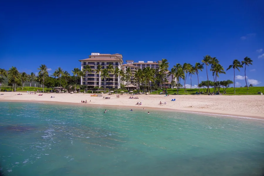 Una playa tropical con agua turquesa, palmeras y un resort frente al mar.