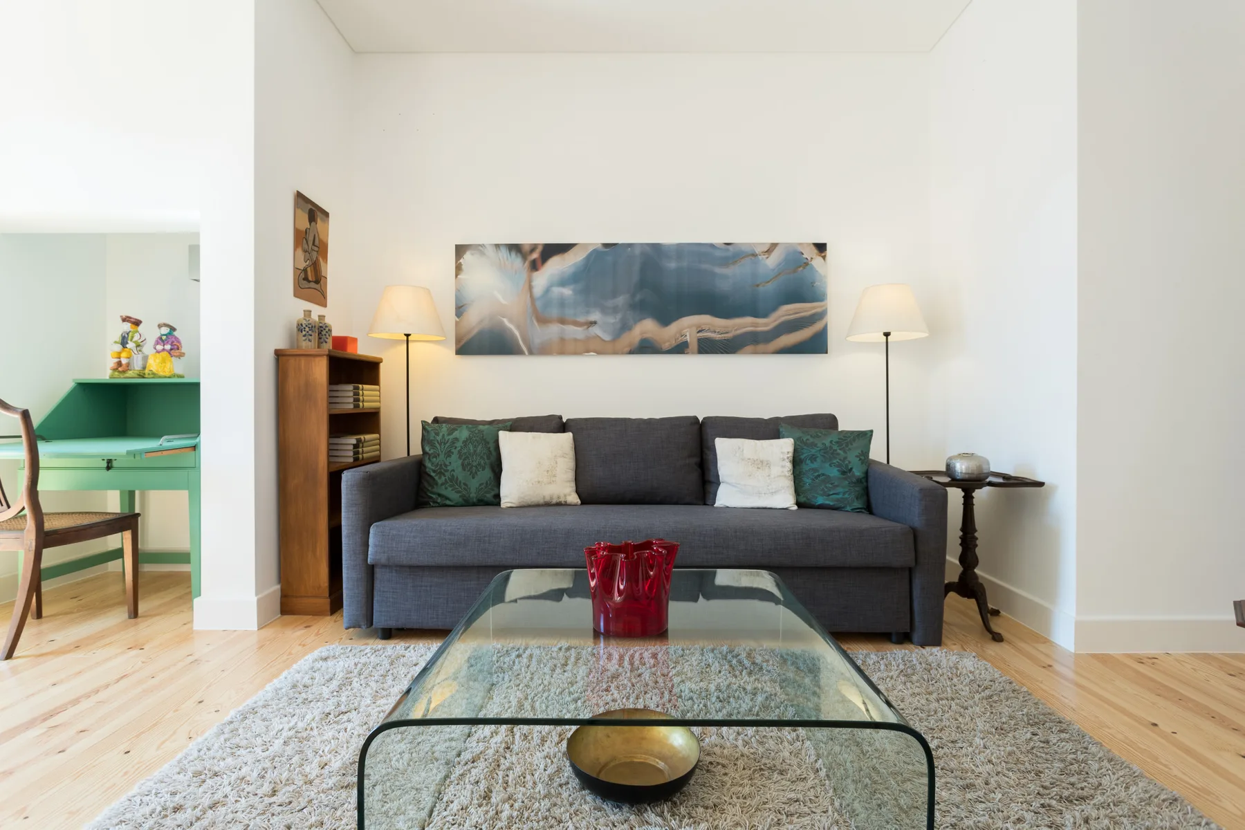 Una sala de estar con sofá gris, mesa de centro de cristal y arte en la pared.