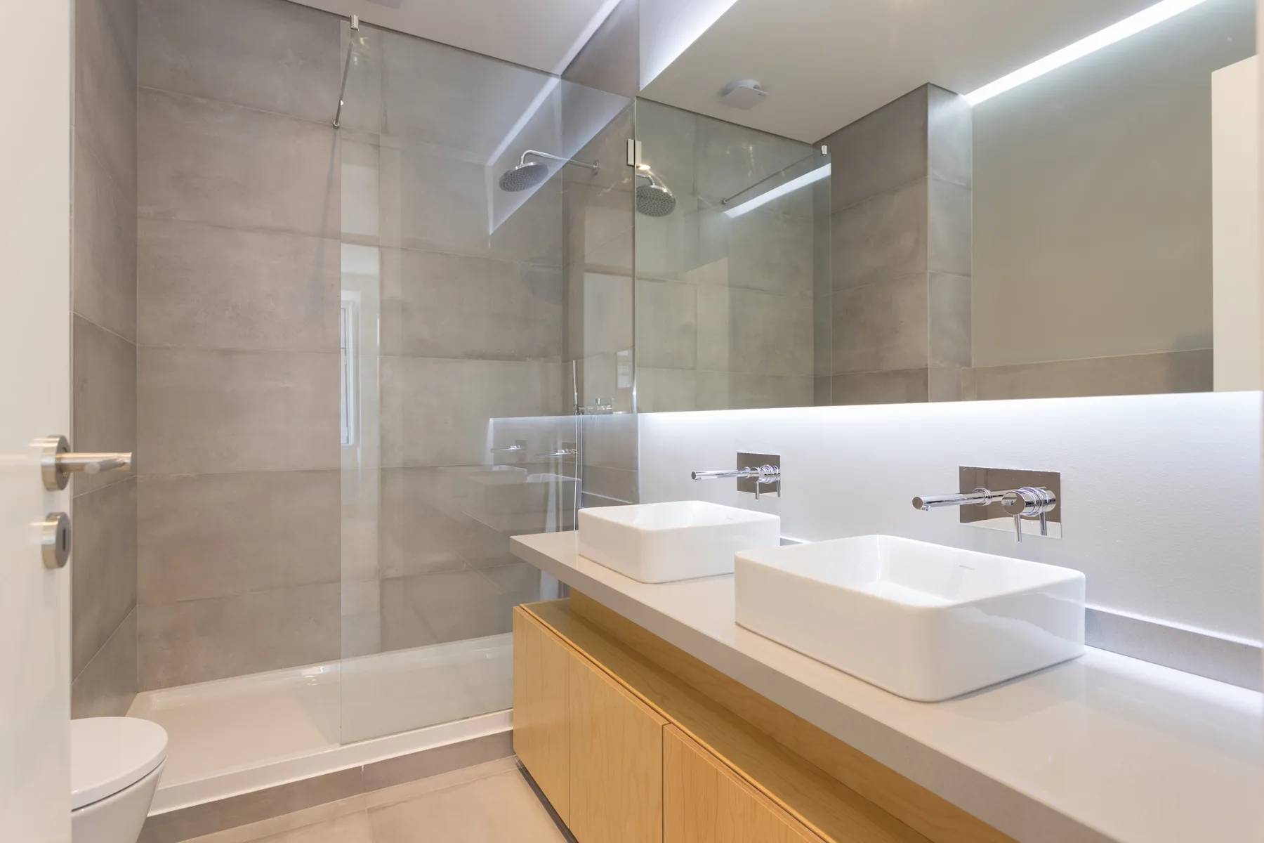 Baño moderno con ducha de vidrio y tocador con dos lavabos.