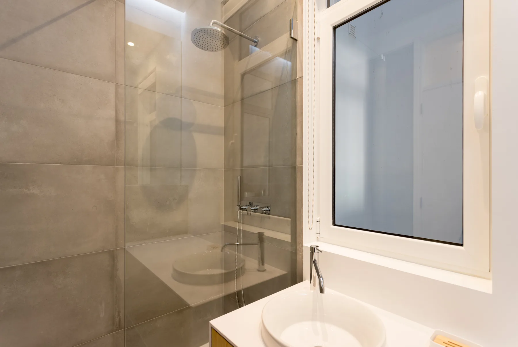 Un baño con una ducha de vidrio y un lavabo bajo una ventana.