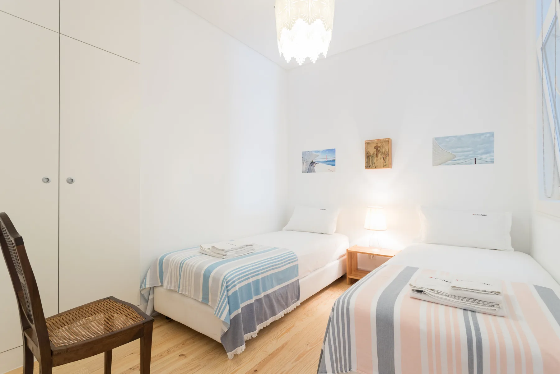 Un dormitorio luminoso con dos camas y cuadros enmarcados sobre ellas.