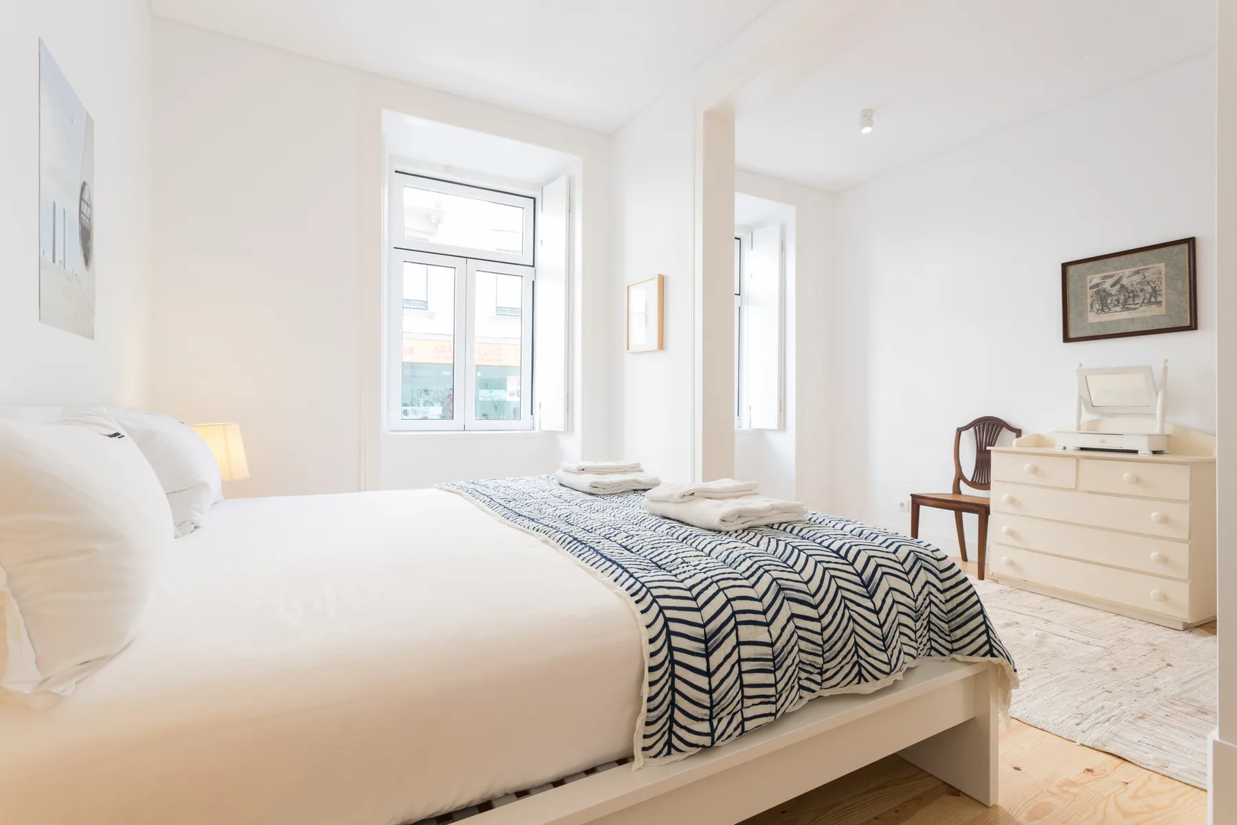 Un dormitorio luminoso con una cama vestida de blanco y una manta estampada.