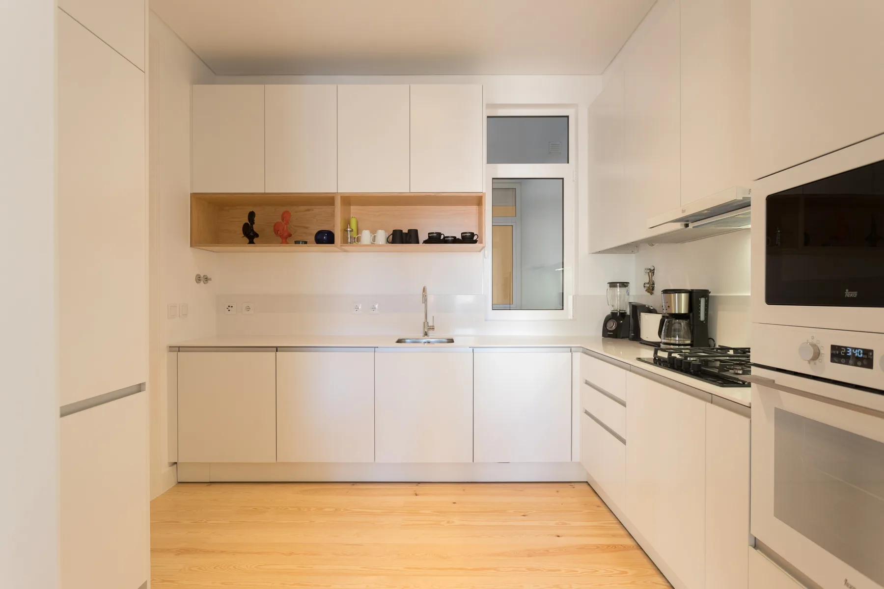 Una cocina moderna y luminosa con armarios blancos, encimera y electrodomésticos integrados.