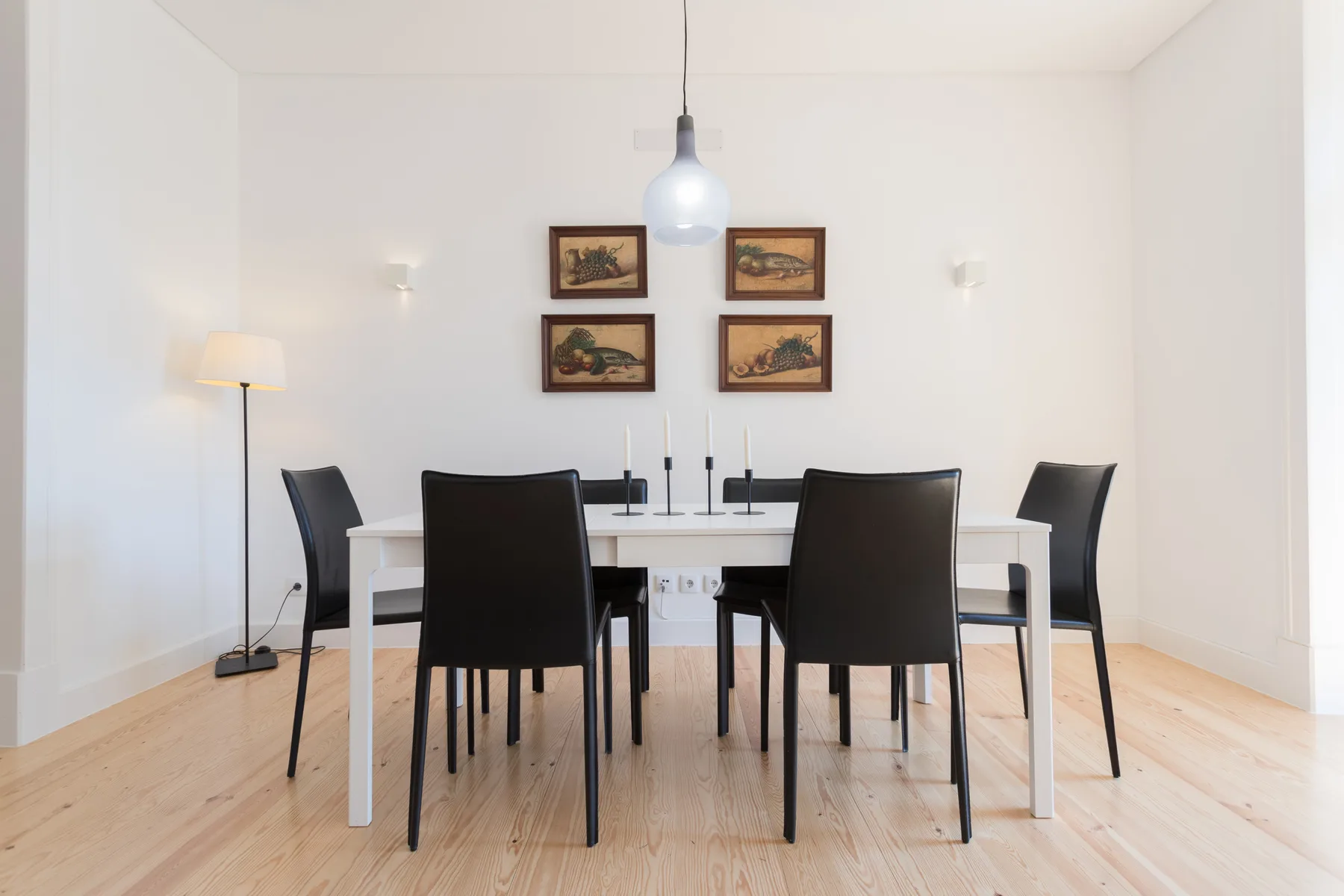 Comedor luminoso con una mesa blanca, asientos oscuros y cuadros enmarcados.