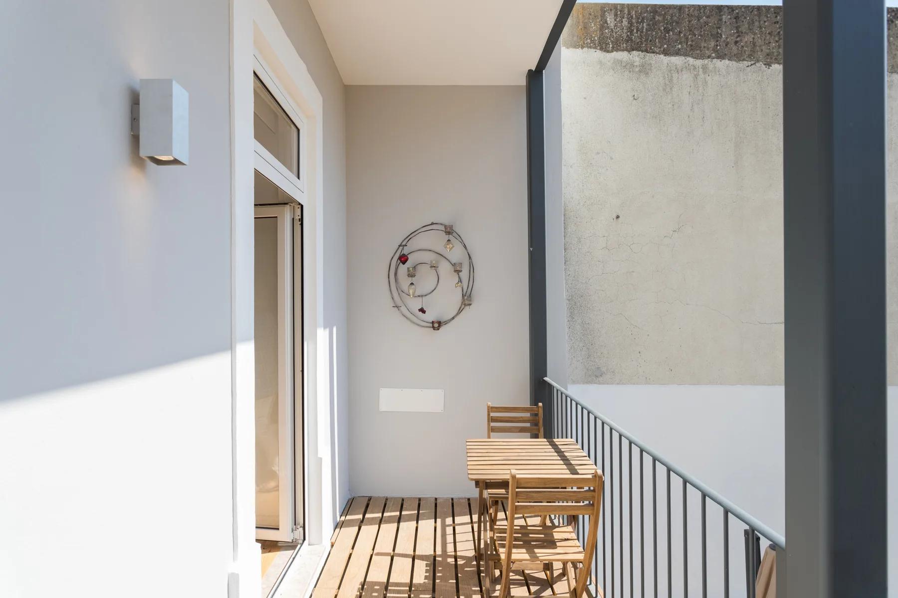Un balcón con una mesa y sillas de madera junto a una pared clara.