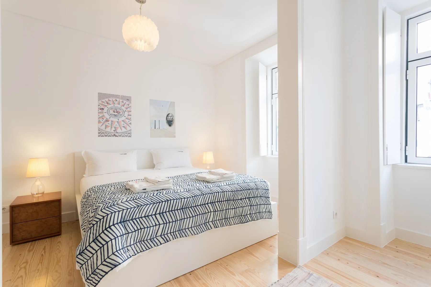 Un dormitorio luminoso con ropa de cama estampada, lámparas de noche y ventanas altas.