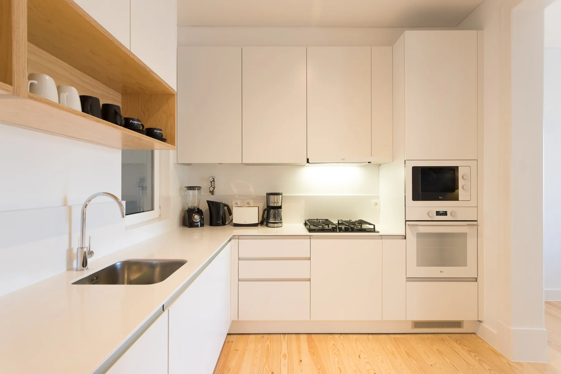 Una cocina moderna y luminosa con armarios blancos y suelo de madera.