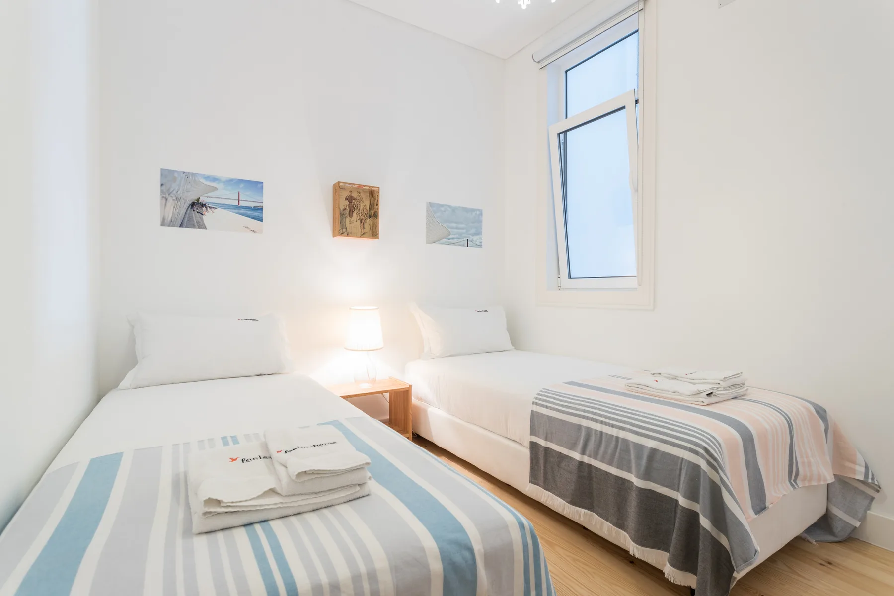 Un dormitorio luminoso con dos camas individuales y pequeños cuadros en la pared.