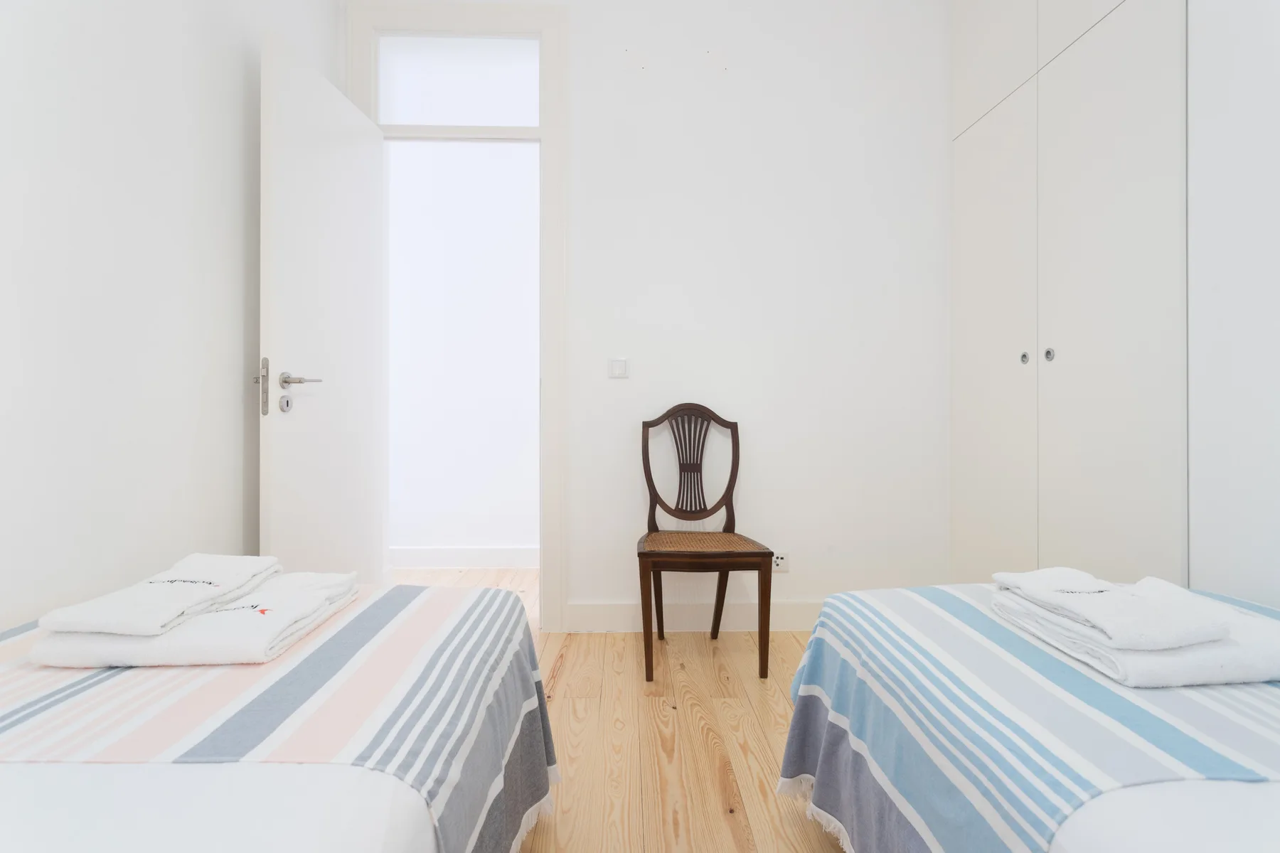 Un dormitorio luminoso con dos camas individuales y una silla de madera entre ellas.