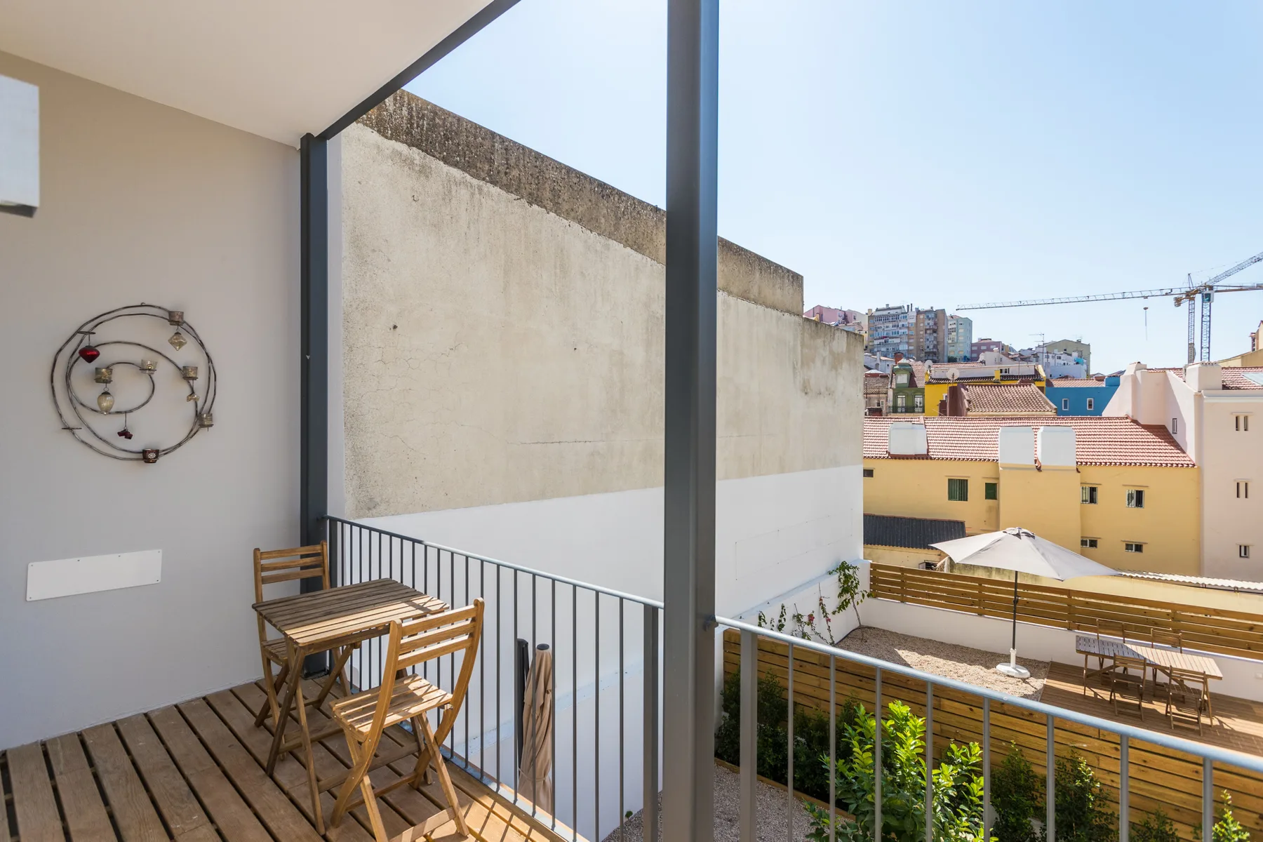 A balcony with wooden seating overlooks nearby rooftops and buildings.