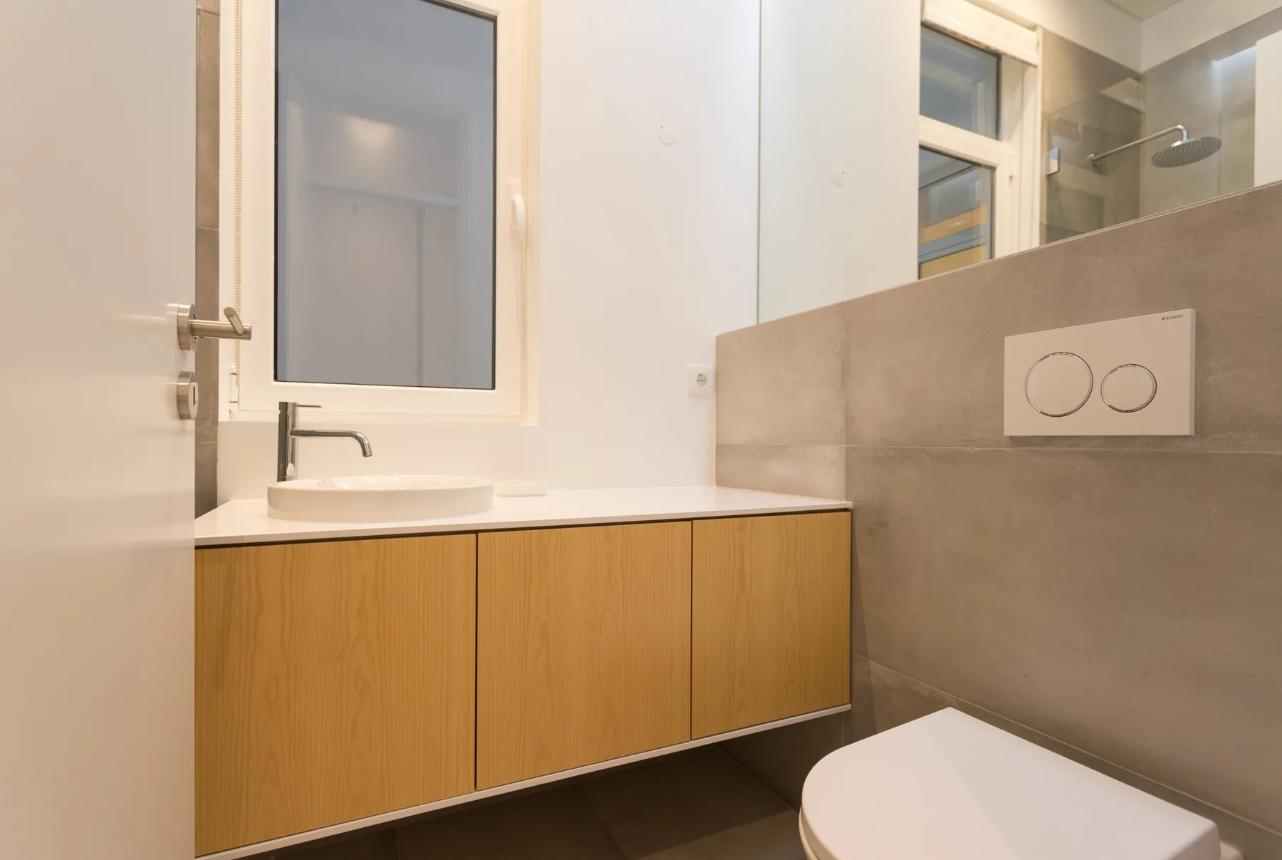 Un baño con lavabo, mueble de tono madera y placa de descarga en la pared.
