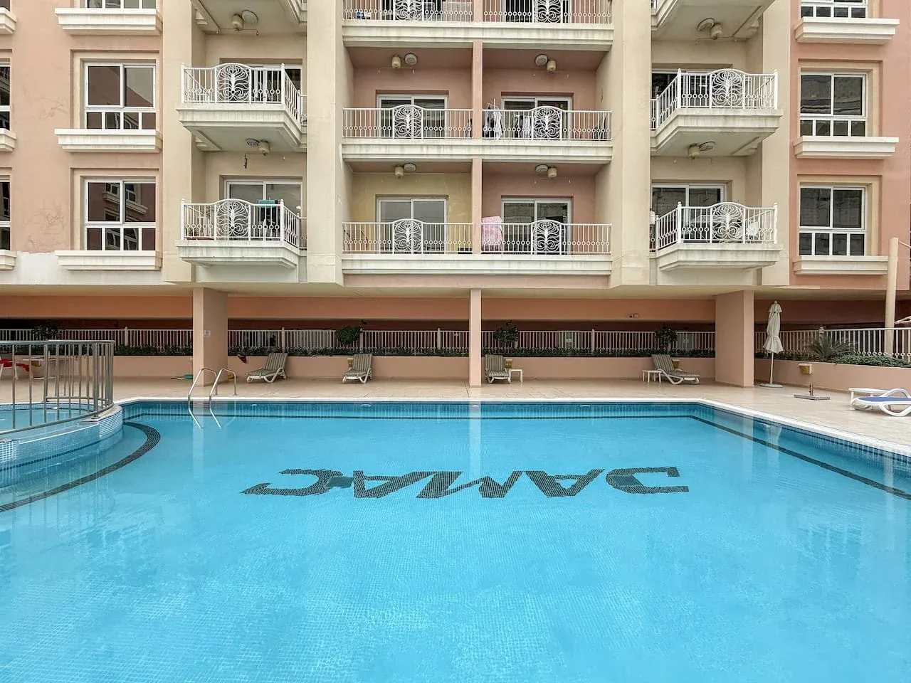 Una piscina al aire libre está frente a un edificio de apartamentos con balcones.