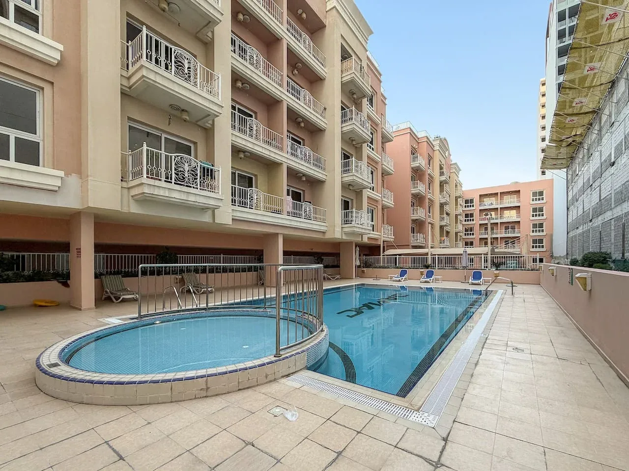 Una piscina al aire libre está junto a un patio pavimentado rodeado de edificios de apartamentos.