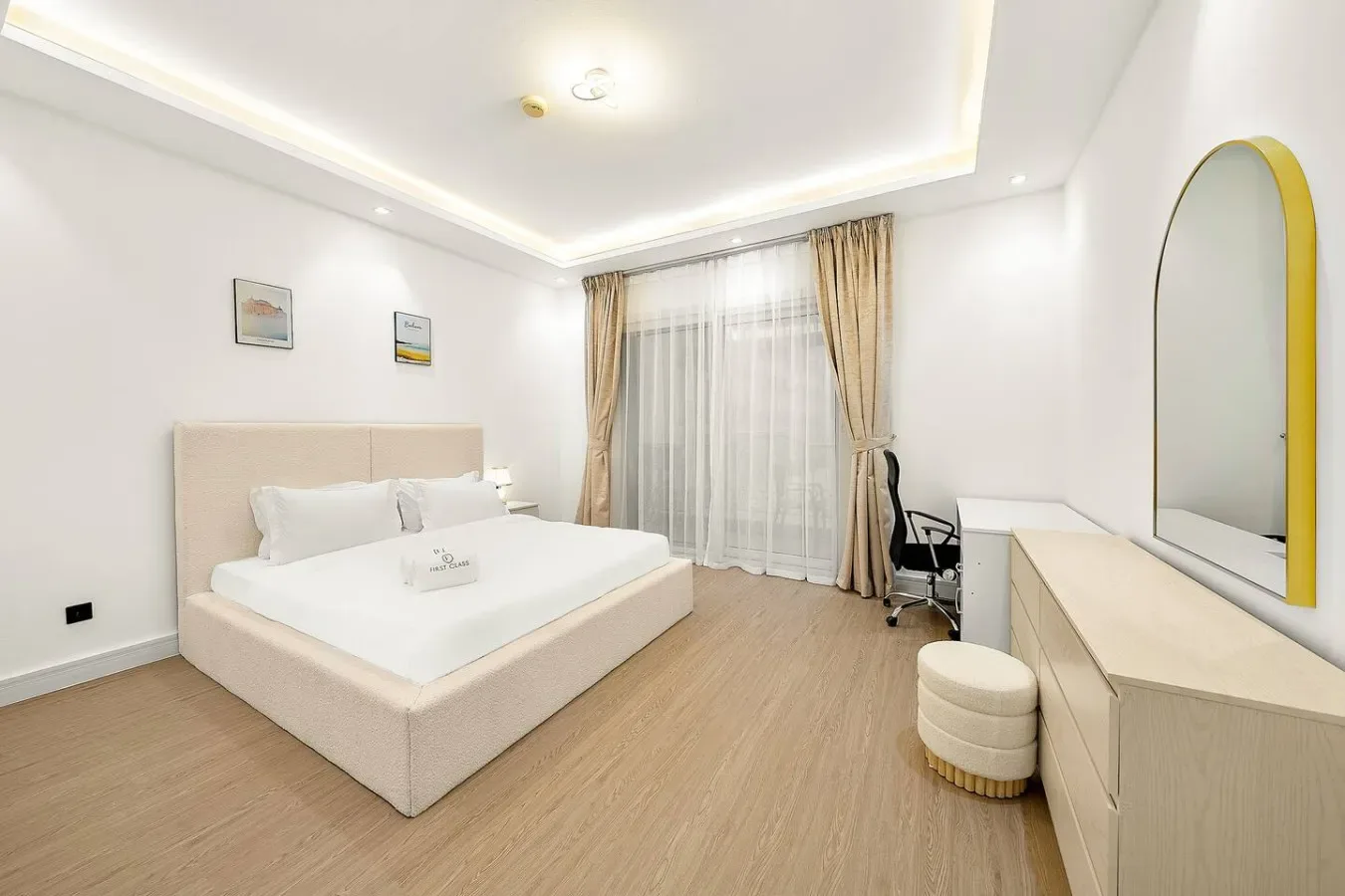 A bright bedroom with a bed, a desk, and curtains over the window.