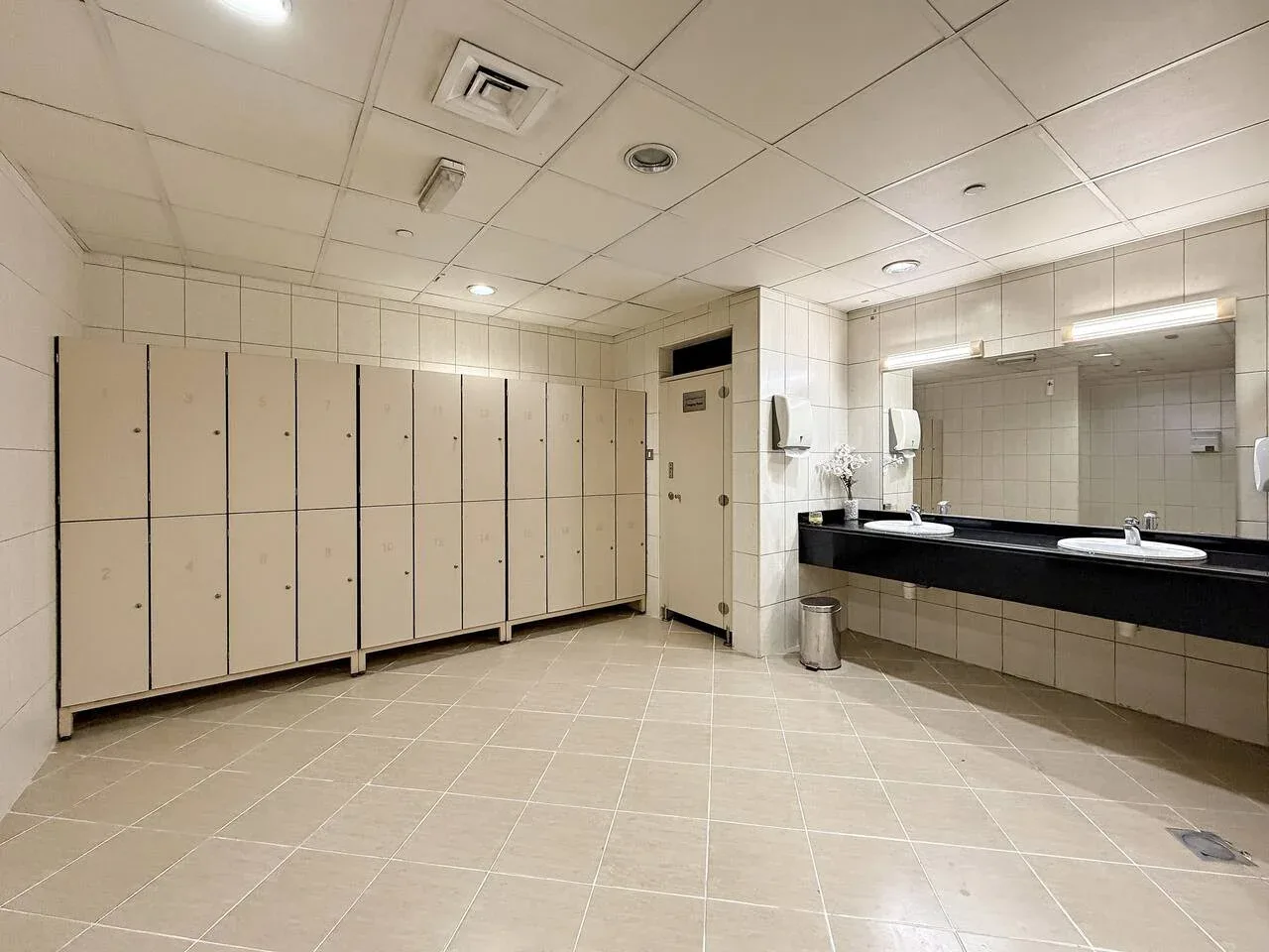 Un baño alicatado con una encimera larga, lavabos y una fila de casilleros.