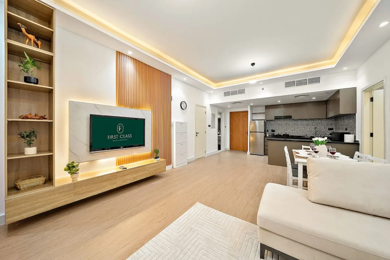 Una sala de estar moderna se abre a una cocina, con un televisor en la pared.