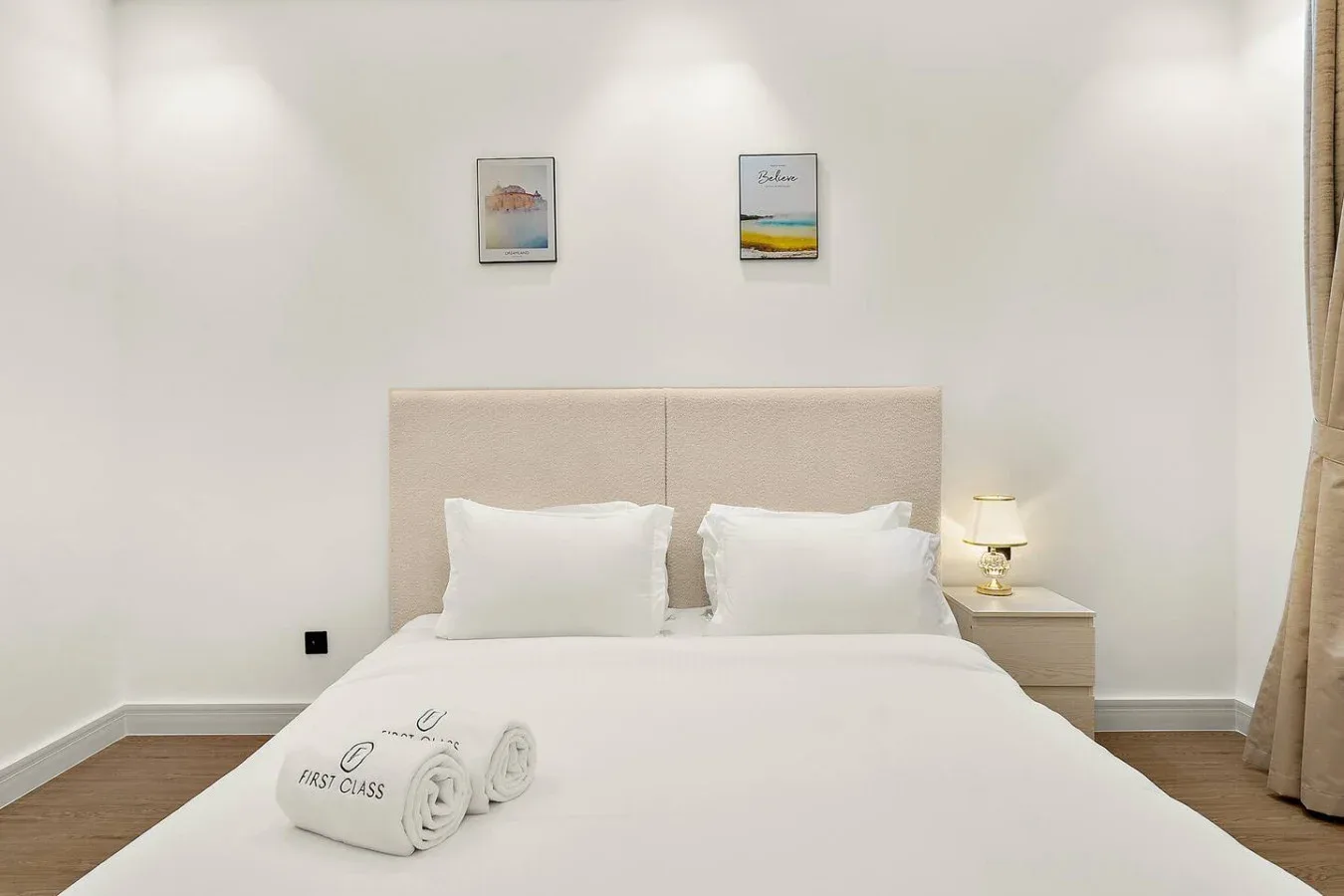 Dormitorio con una cama bien hecha, una mesita de noche y cuadros enmarcados.