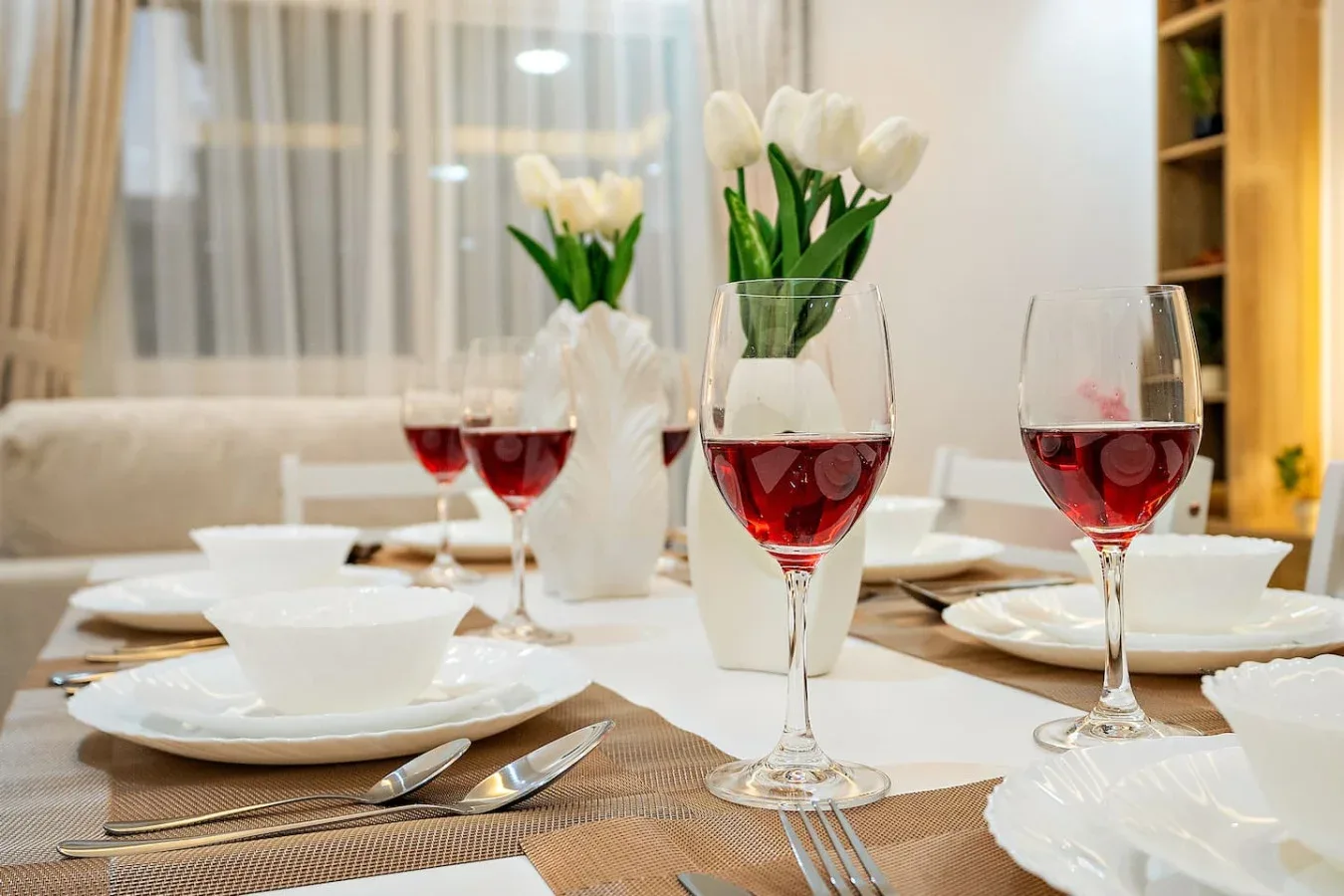 Una mesa de comedor está puesta con platos, copas de vino tinto y flores.