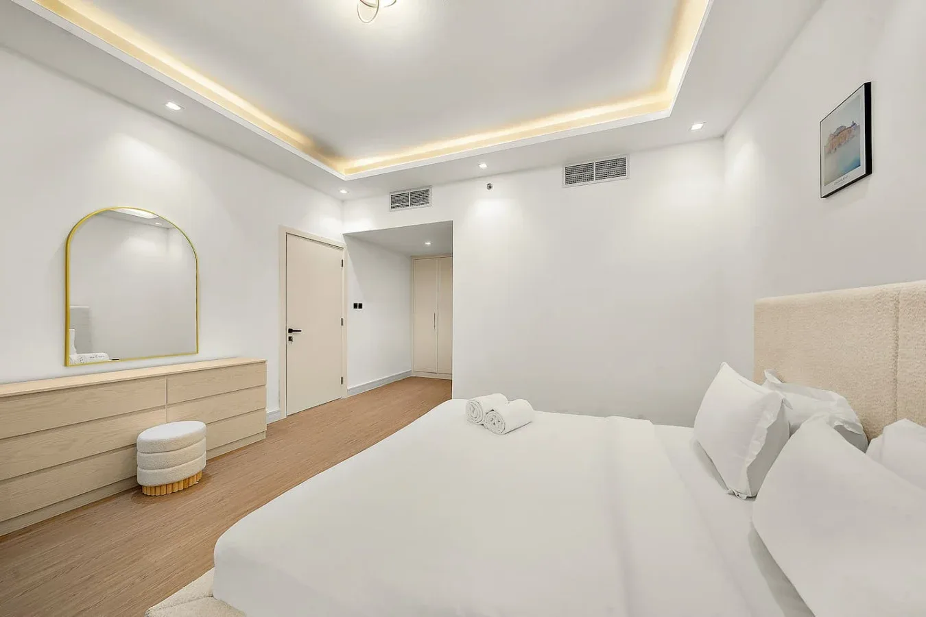Un dormitorio luminoso con una cama bien tendida y una cómoda con espejo.