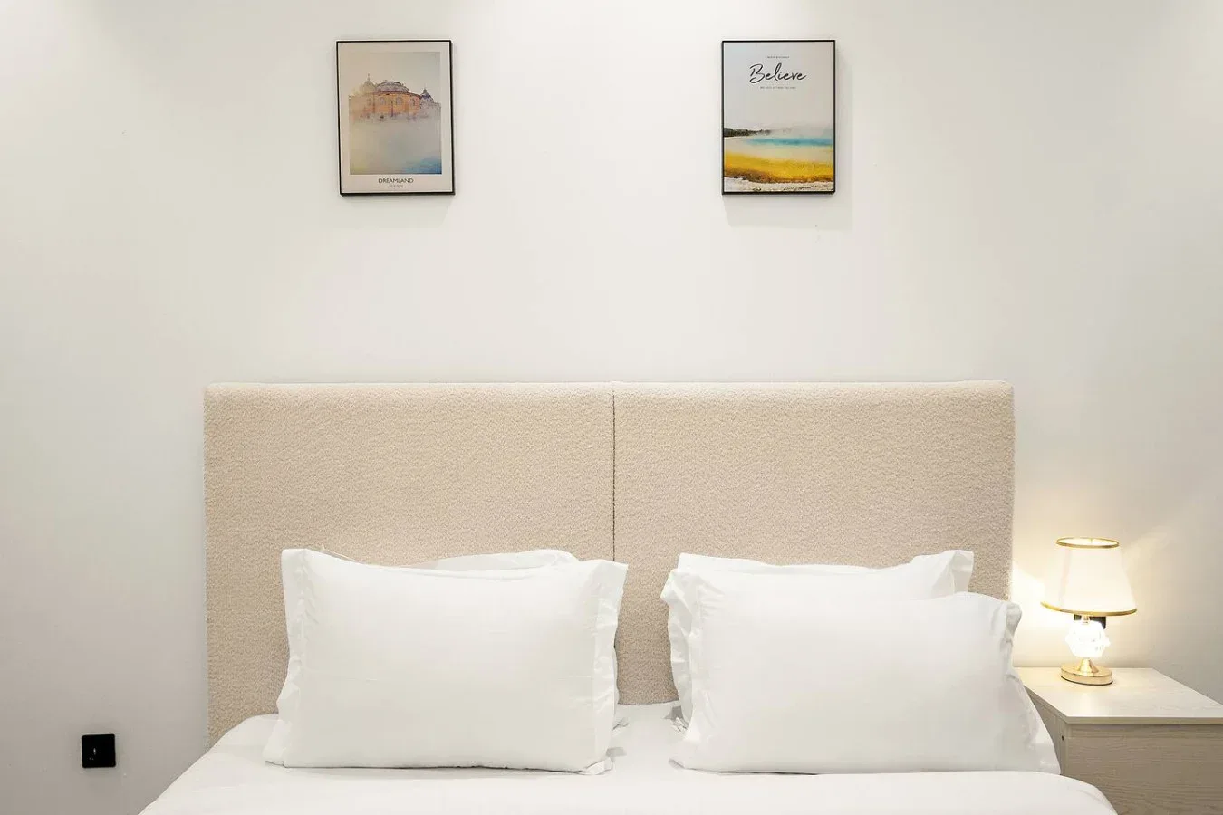 Un dormitorio con ropa de cama blanca y cuadros enmarcados sobre la cama.