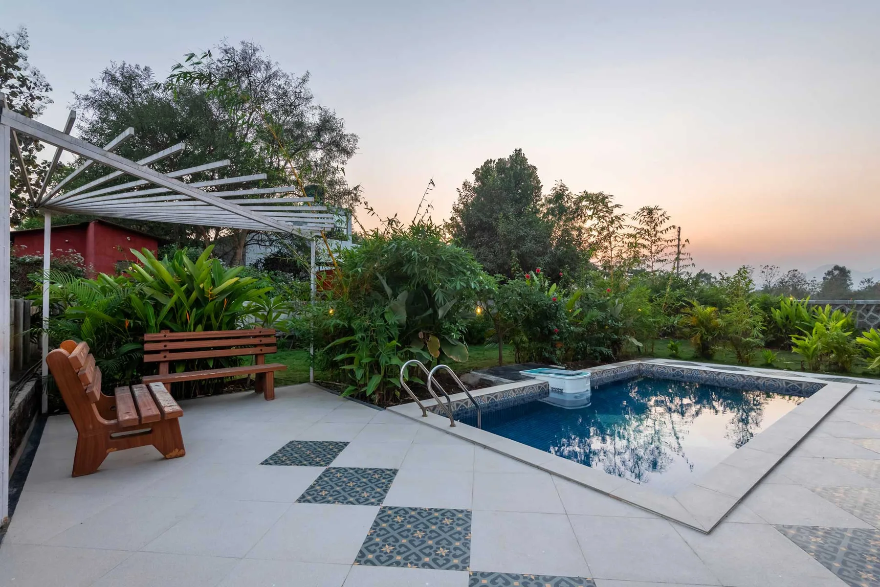 Una piscina al aire libre está junto a un patio embaldosado rodeado de vegetación frondosa.