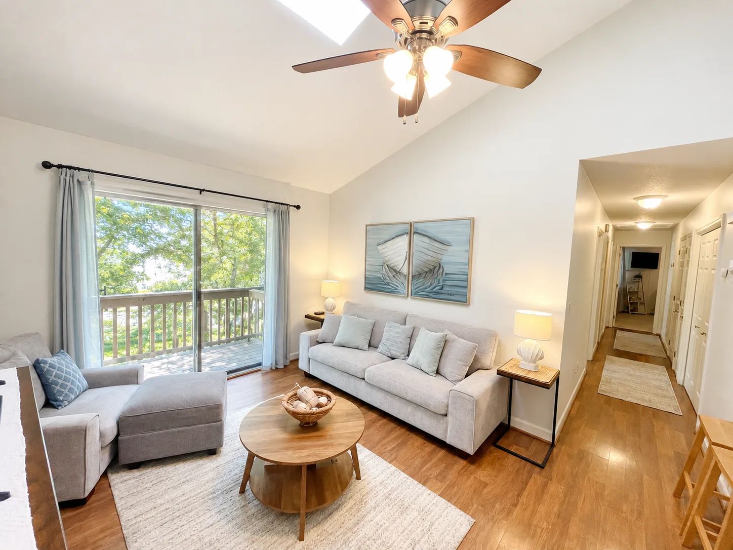 A bright living room with a seating area and large windows overlooking leafy trees.