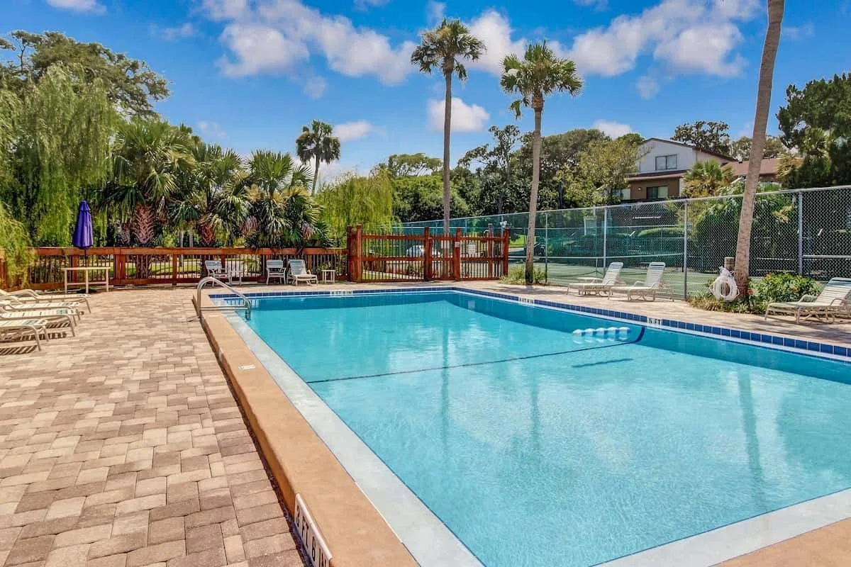 An outdoor swimming pool is surrounded by a paved deck and lounge chairs.