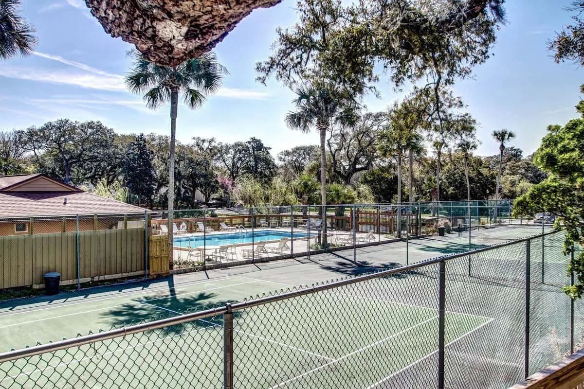 An outdoor tennis court beside a swimming pool, surrounded by trees.