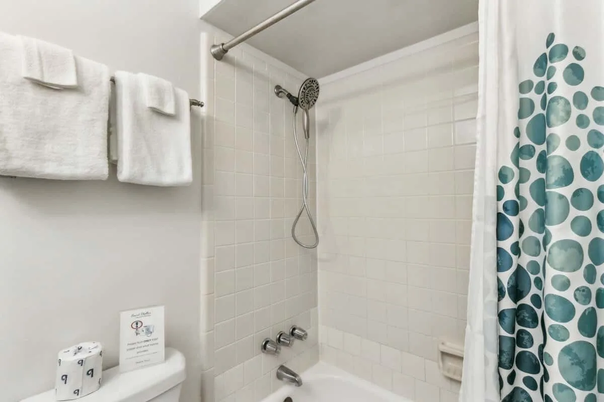 A tiled bathroom shower with a patterned curtain and towels hanging nearby.