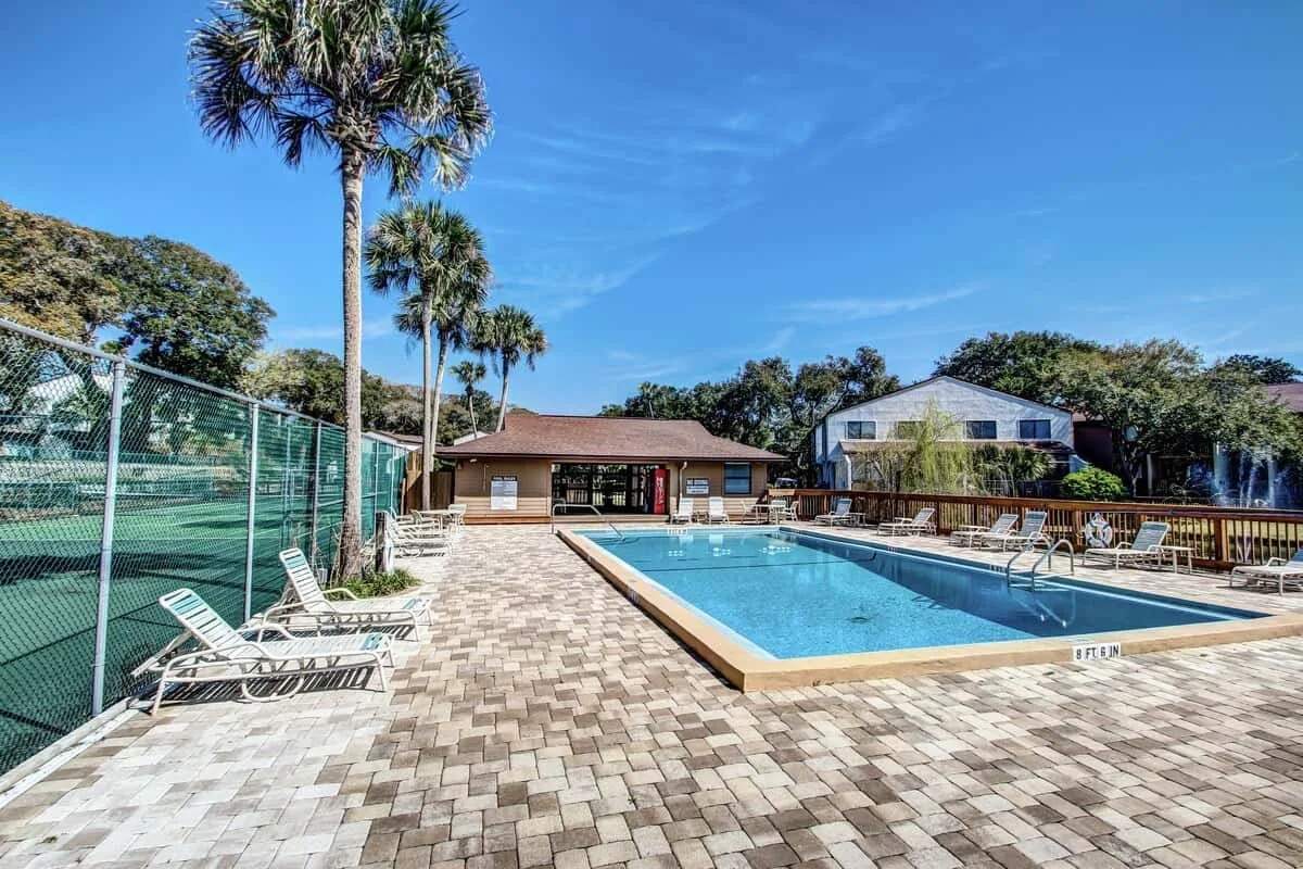 An outdoor swimming pool is surrounded by paved decking and lounge seating.