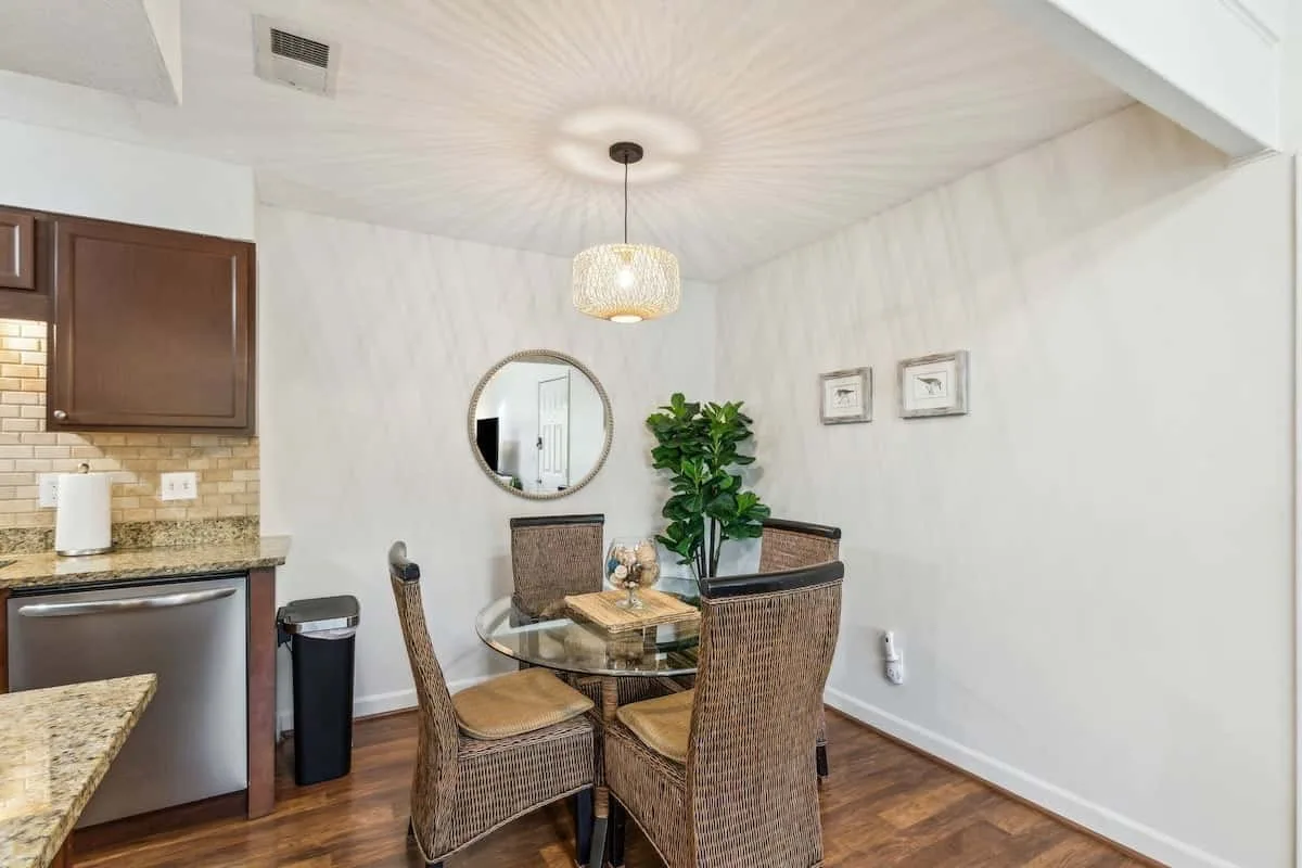 A dining area with wicker seating around a glass table beside the kitchen.