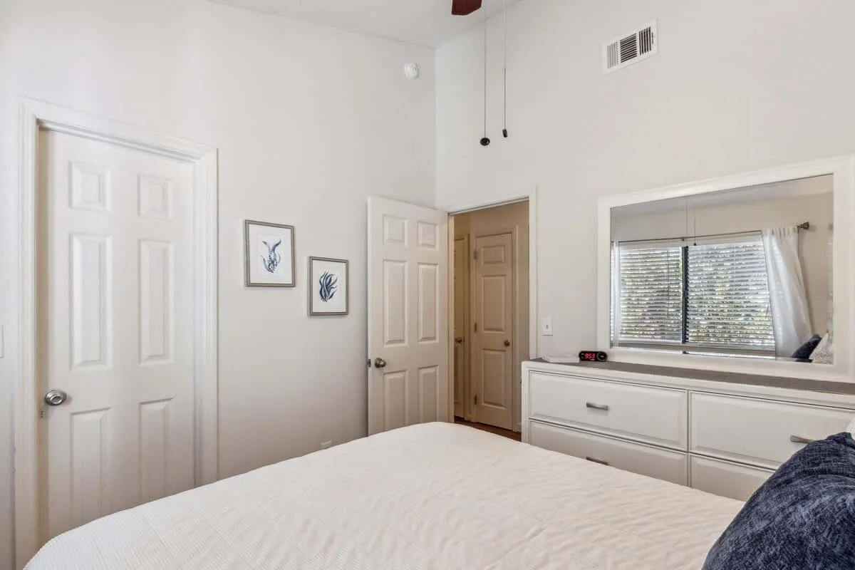 A bedroom with a bed, framed pictures, and a window above built-in drawers.