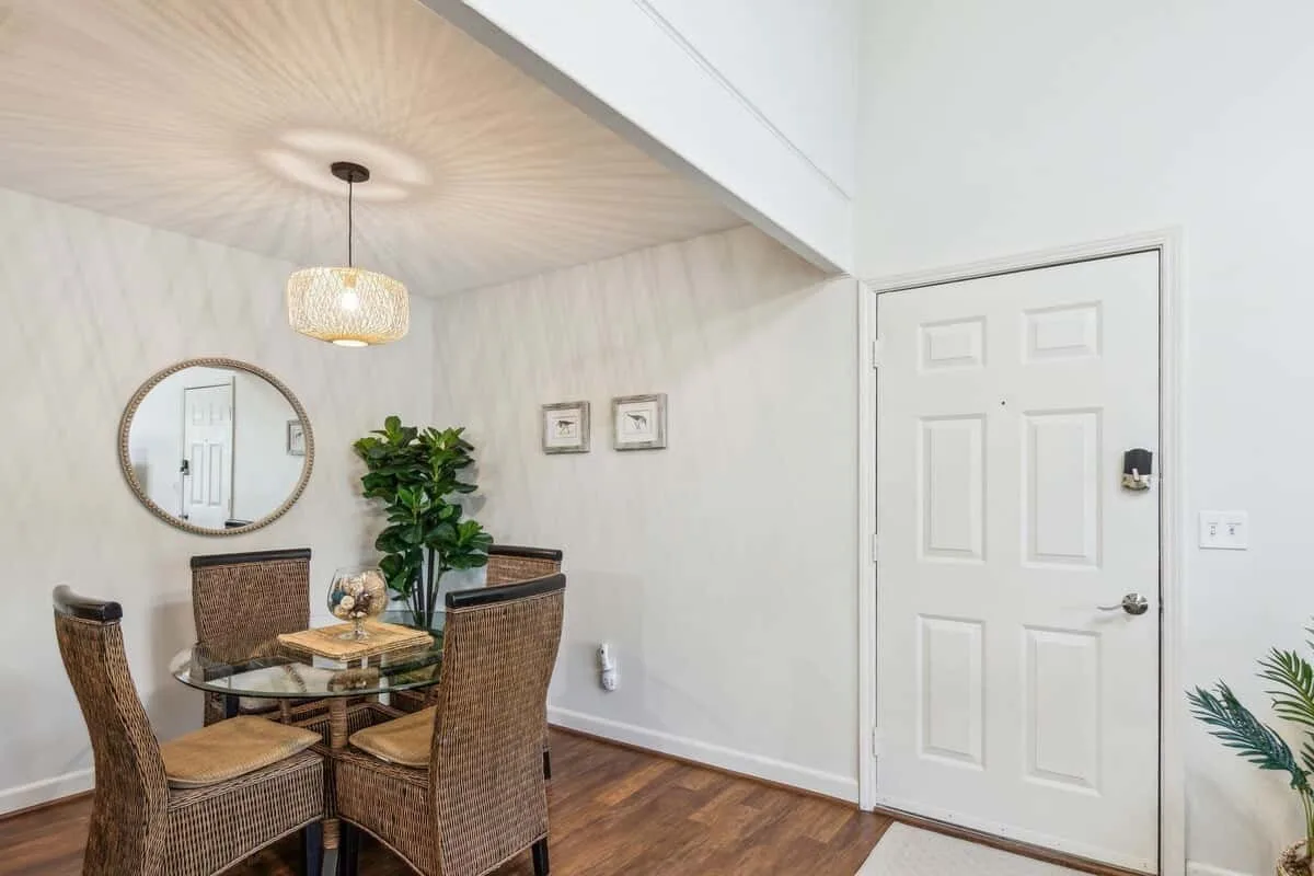 A dining area with wicker seating, a glass table, and a round wall mirror.