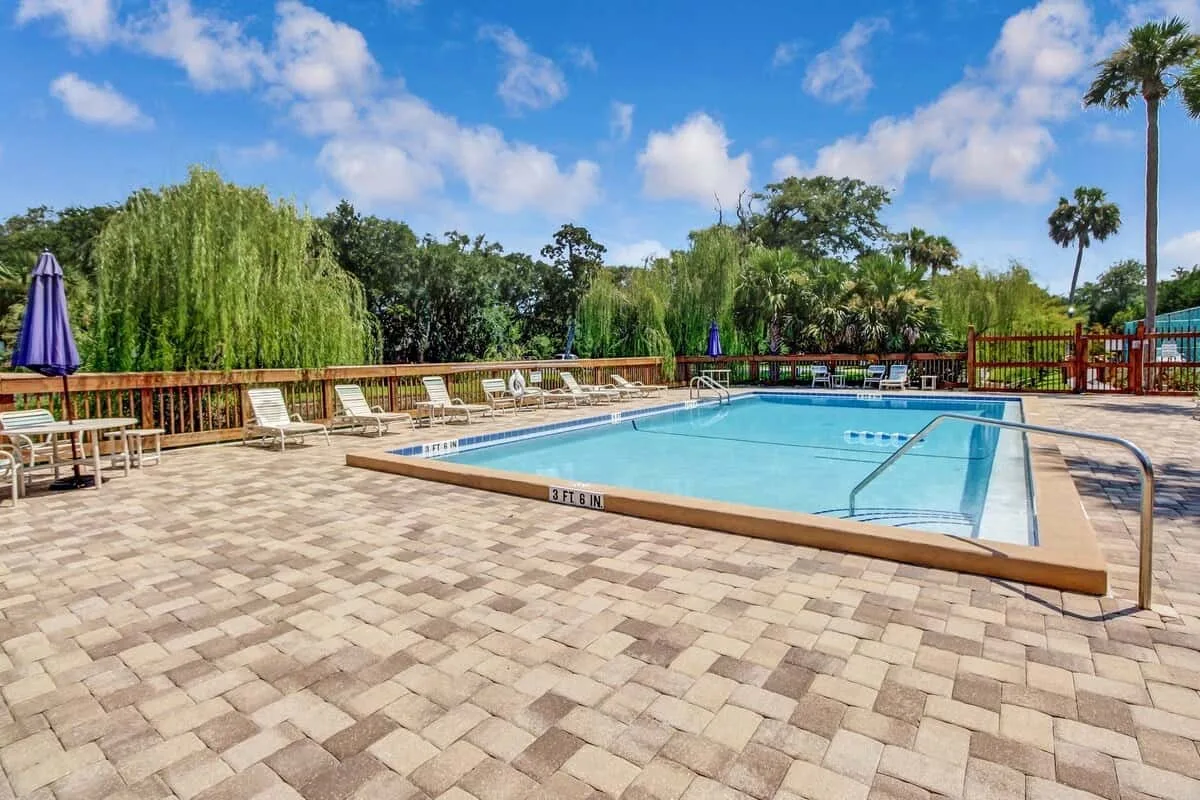 An outdoor swimming pool is surrounded by a paved deck and lounge seating.