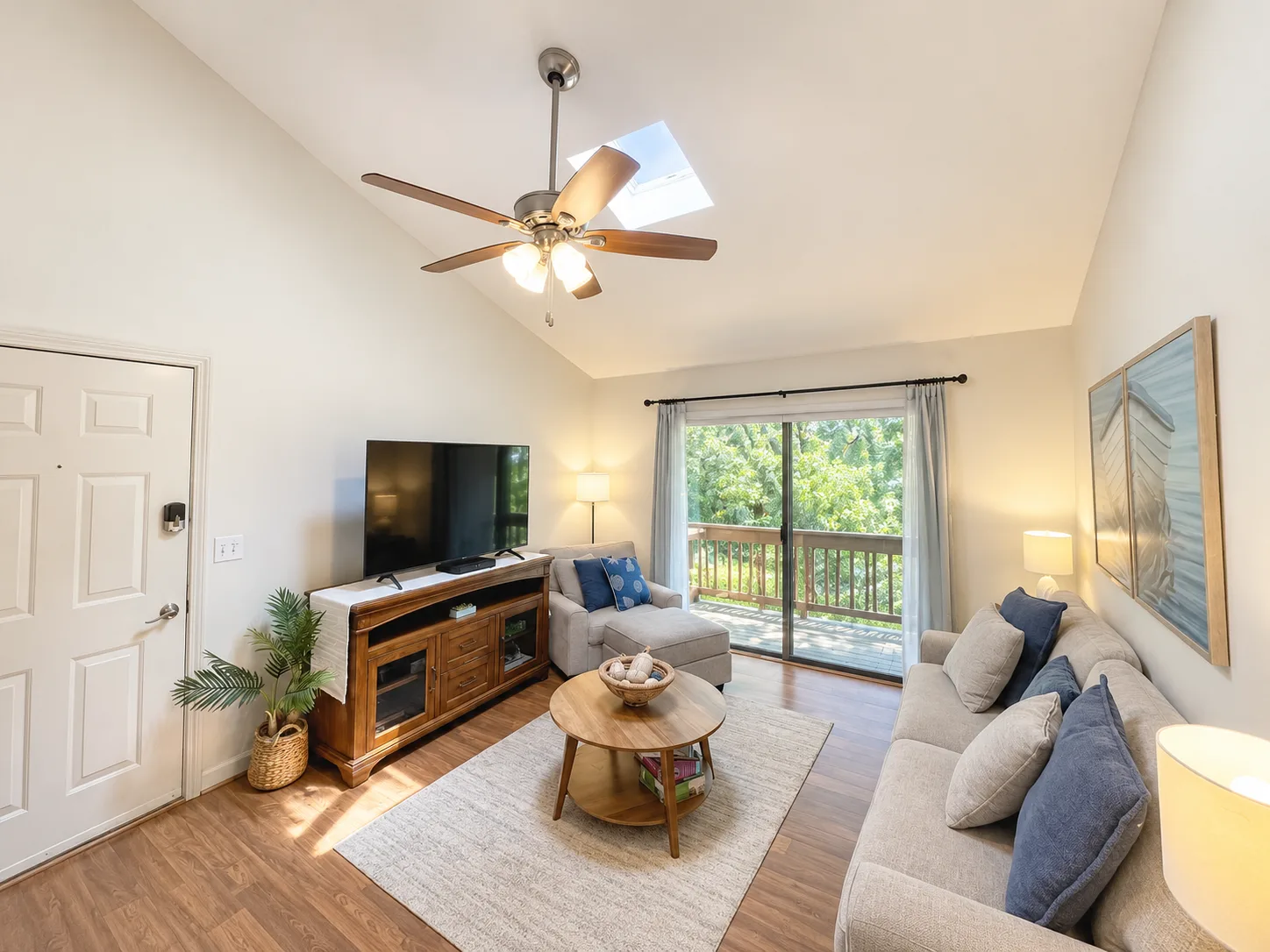 A bright living room has seating, a television, and sliding glass doors opening to a balcony.