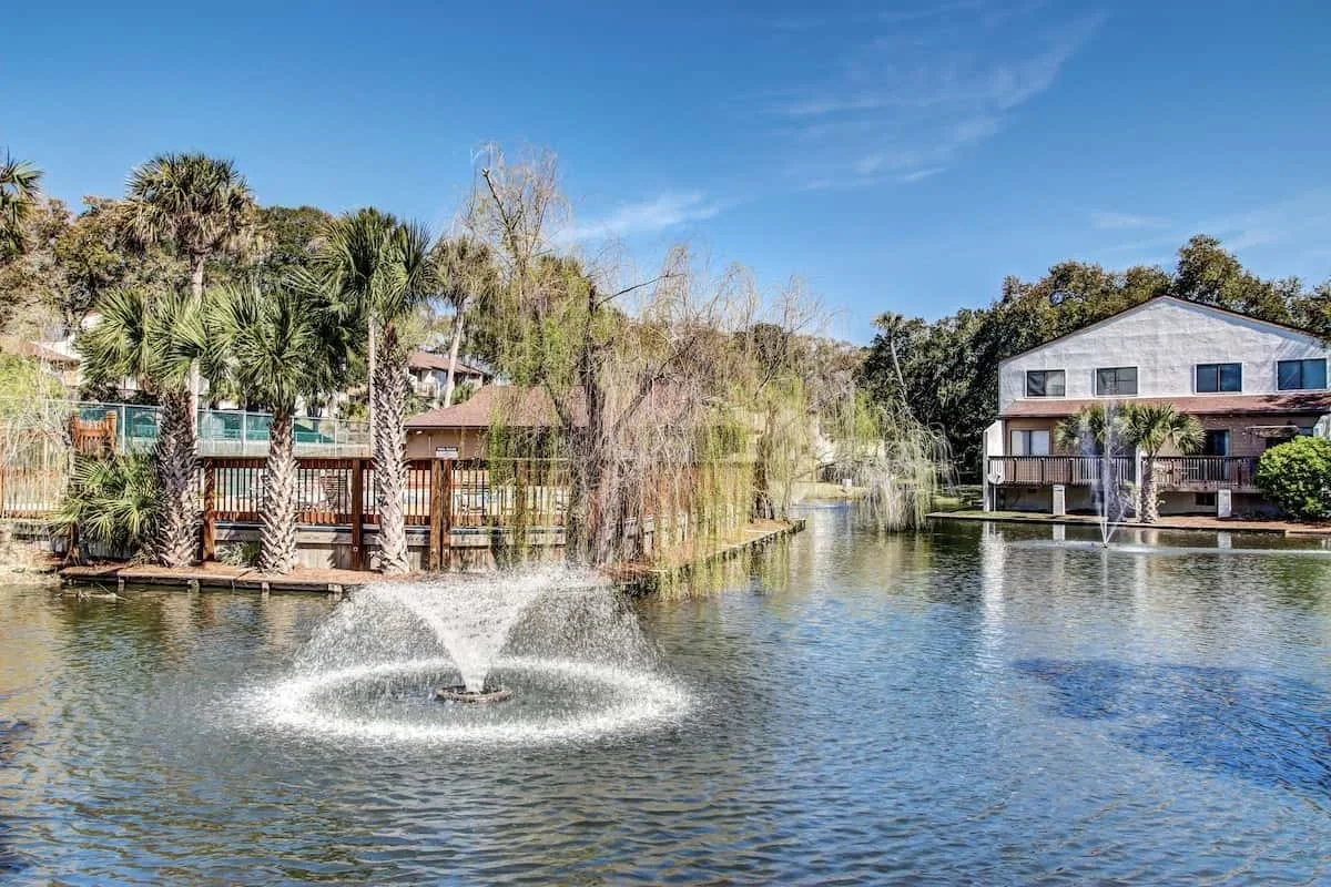 Waterfront buildings and trees line a pond with a fountain.