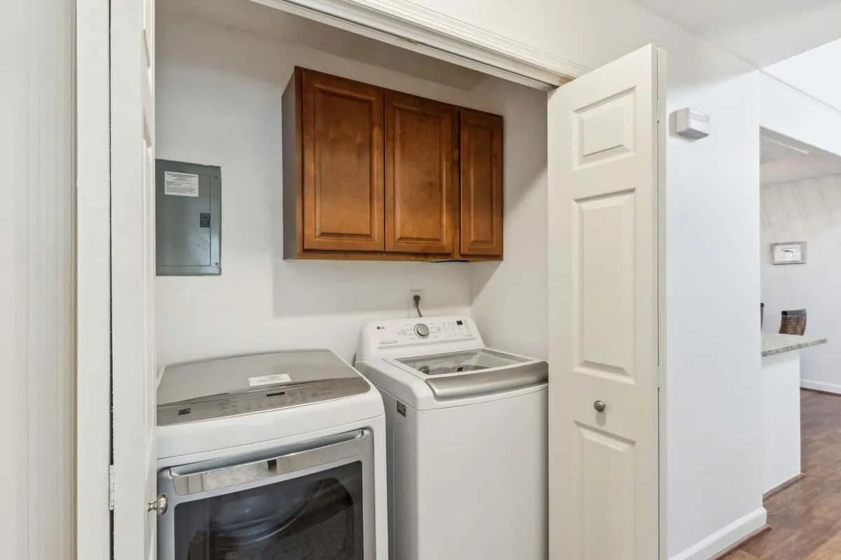 A laundry area with a washer, dryer, and overhead wooden cabinets.