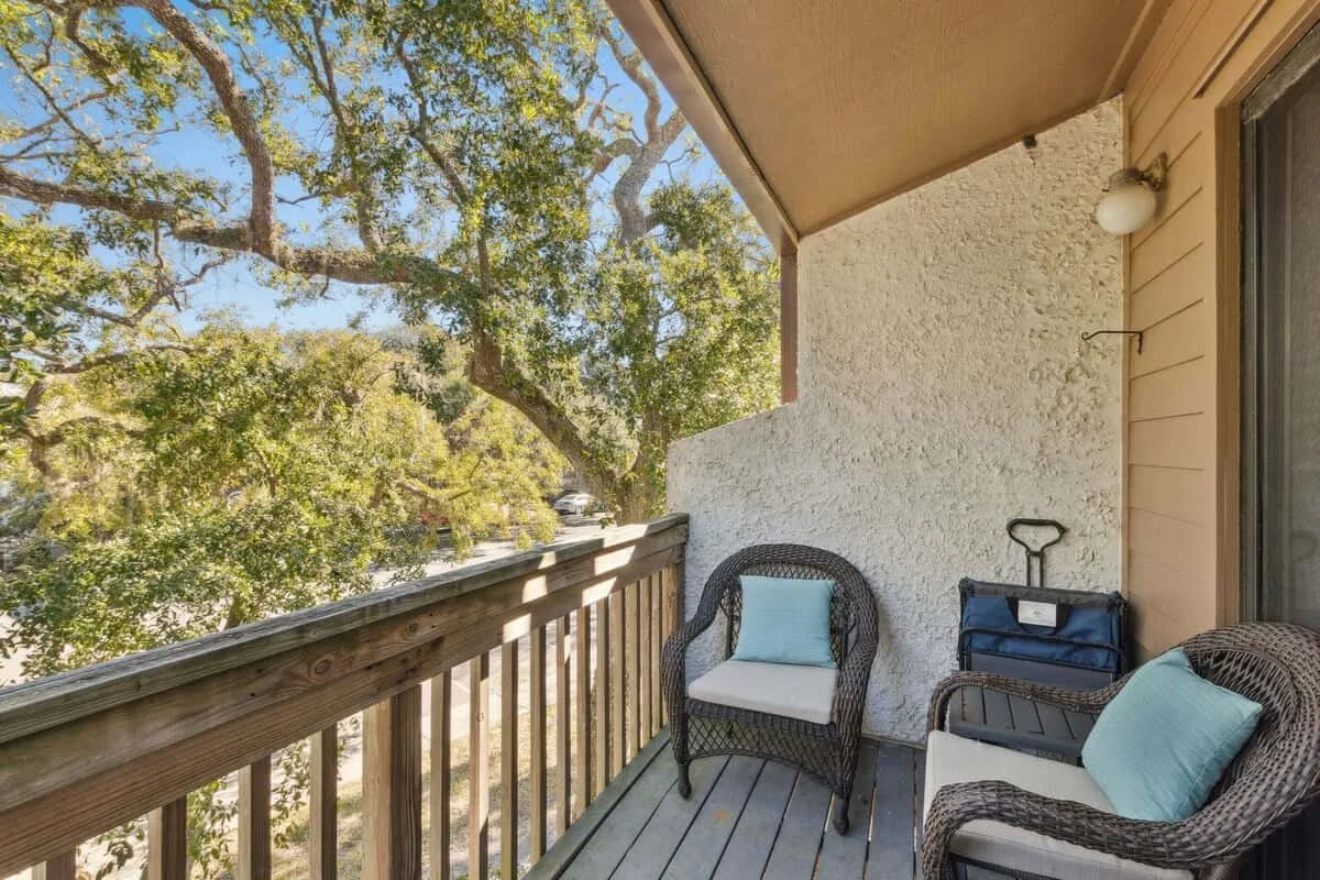 A small balcony with outdoor seating and leafy trees beyond the railing.