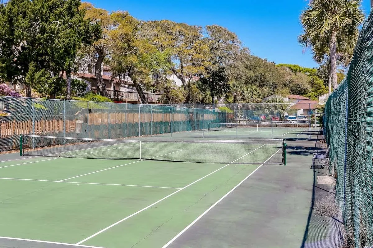 An outdoor tennis court with green playing surfaces and surrounding trees.