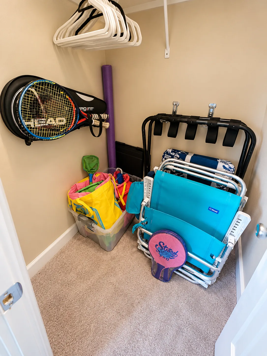A carpeted storage closet holds sports equipment, beach bags, and folded chairs.