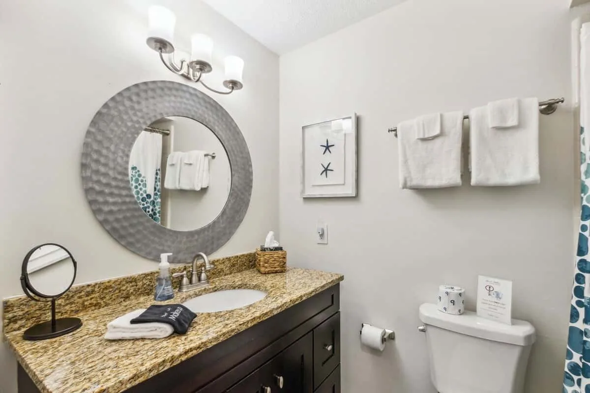 A bathroom vanity with a round mirror and white towels on the wall.