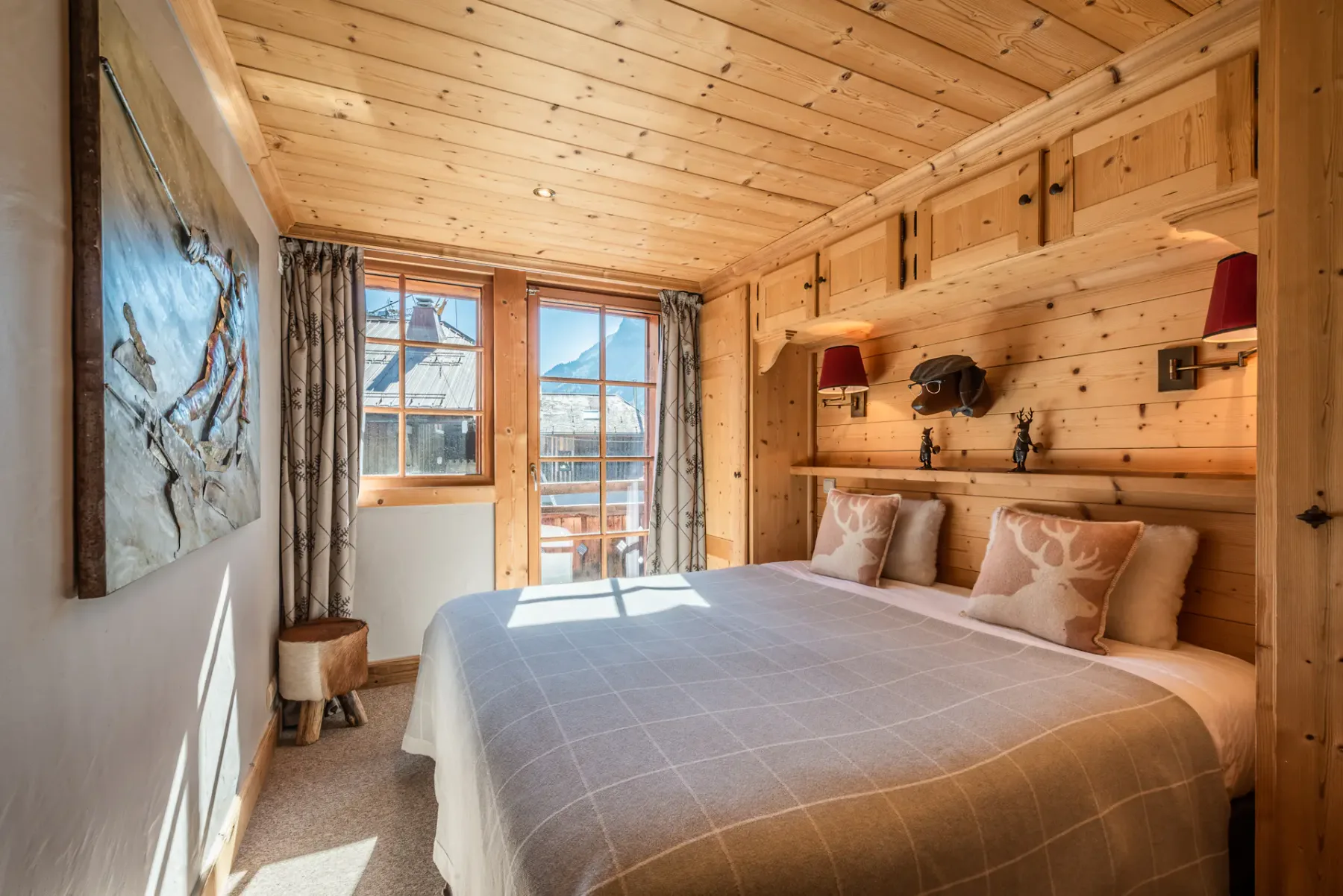 A bedroom with a made bed, wood-paneled walls, and a window overlooking the mountains.