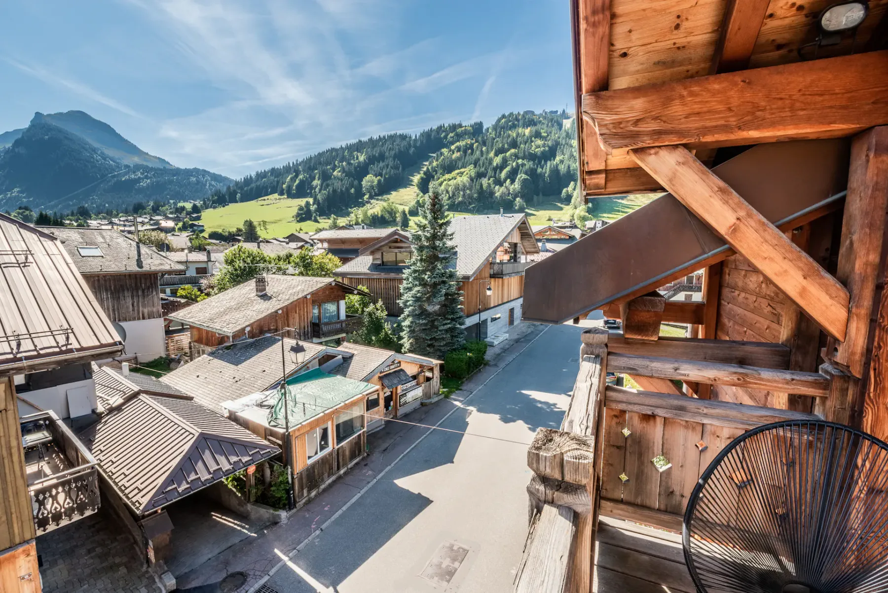 A mountain village street is lined with buildings, with wooded slopes in the background.