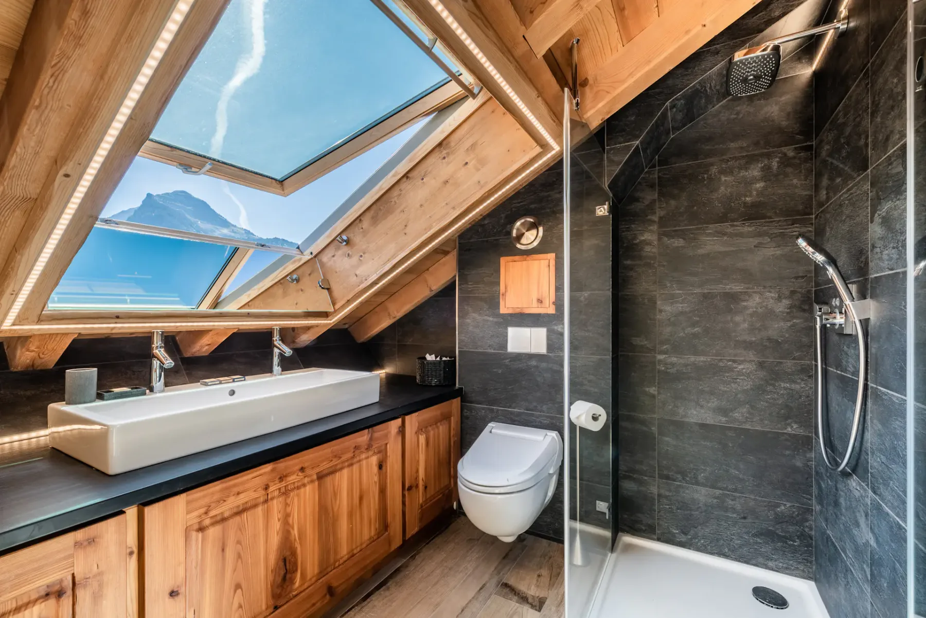 A bathroom with a bathtub, toilet, and glass-enclosed shower beneath skylights.