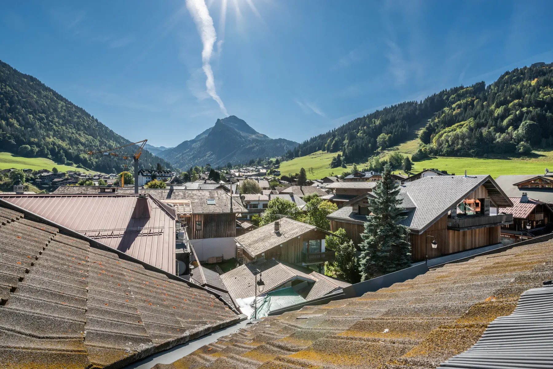 A mountain village spreads across a green valley beneath a bright blue sky.