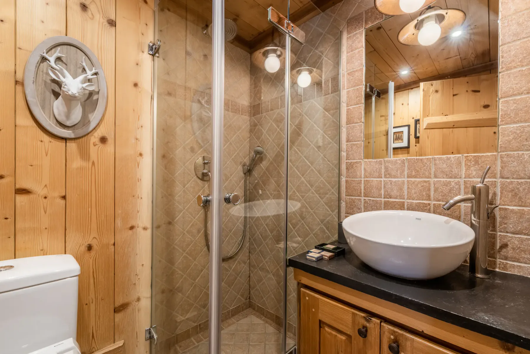 A tiled bathroom with a shower and a white basin on a wooden vanity.