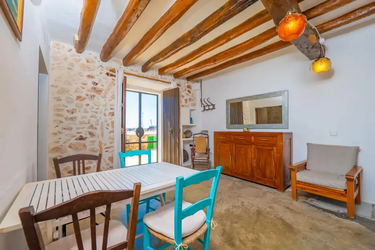 Zona de comedor y estar con una mesa de madera, sillas de colores y un aparador.