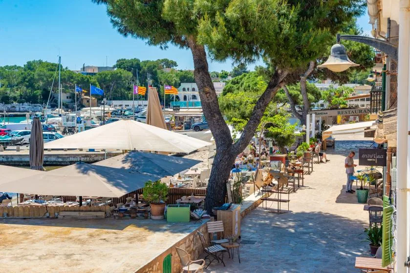 Una terraza junto al agua ofrece mesas al aire libre a la sombra, frente a una marina.