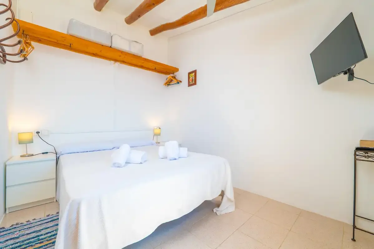 Un dormitorio luminoso con una cama bien tendida y un televisor en la pared.