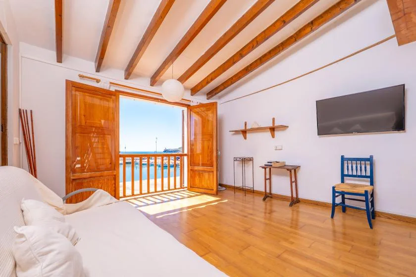 Una habitación luminosa con una cama, un televisor en la pared y puertas abiertas al balcón.